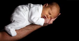 Man's extended arm holding a sleeping baby.